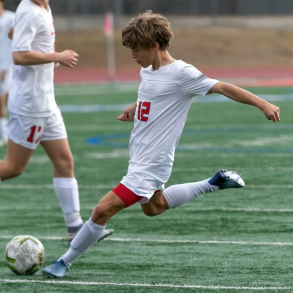 Un jeune joueur en tenue blanche frappe dans un ballon lors d’un match de football, illustrant l’intensité et l’engagement du stage de football en Irlande.