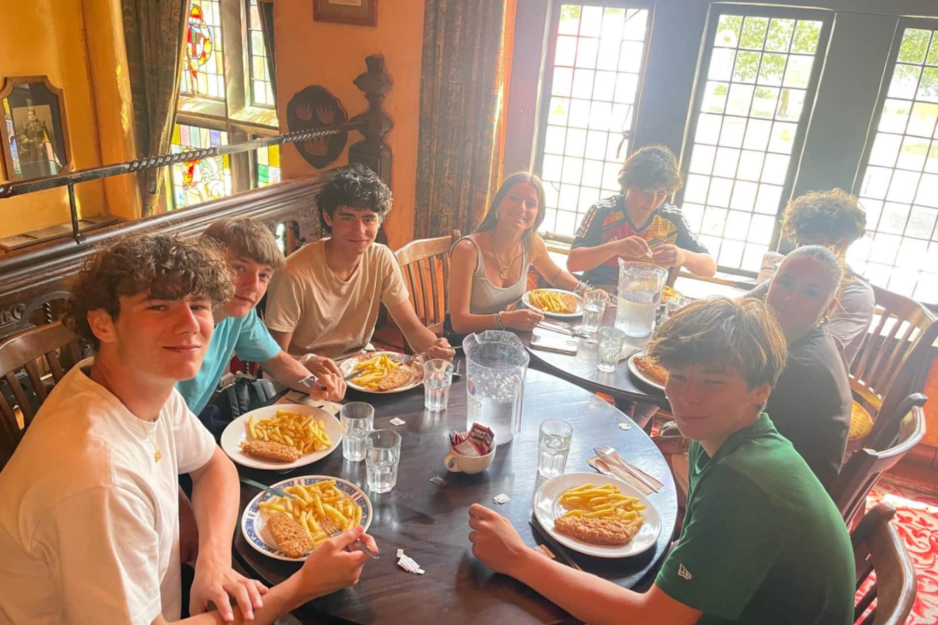 Adolescents assis autour d'une table de pub en bois, mangeant du fish and chips.