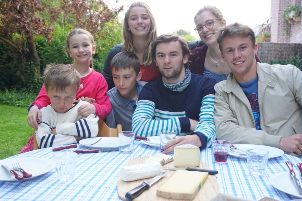Une famille d’accueil française partage un repas d’immersion avec un lycéen international dans un jardin en France.