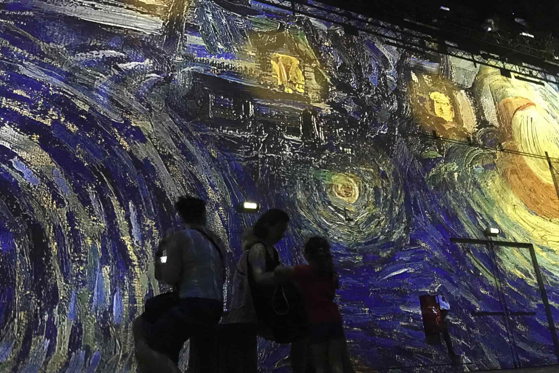 Visitors surrounded by colourful digital art projections inside the Atelier des Lumières in Paris