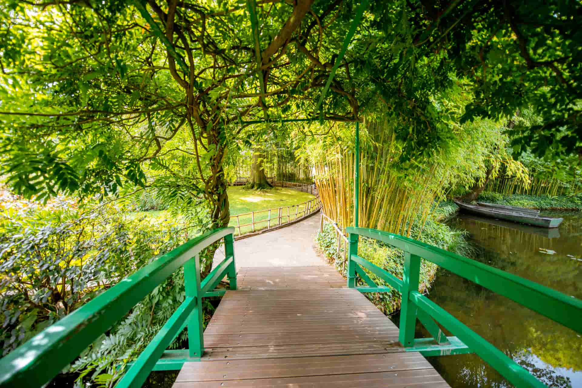 Green Japanese bridge surrounded by trees and lush vegetation in Claude Monet's garden in Giverny